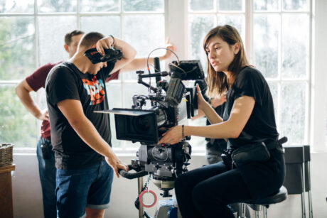 Female director of photography with a camera on a movie set. Professional videographer on the set of a movie, commercial or TV series. Filming indoors, studio